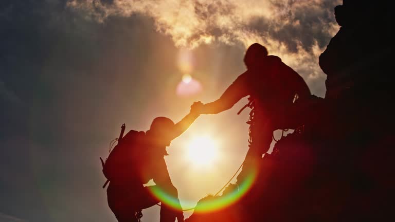 Silhouette of two mountaineers climbing the top at sunset