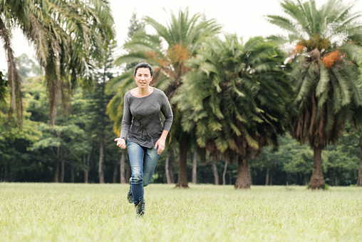Brunette woman wearing casual clothes enjoying her free time in a city park, running in a grass field. 35-39 years old caucasian ethnicity. Retouched image.