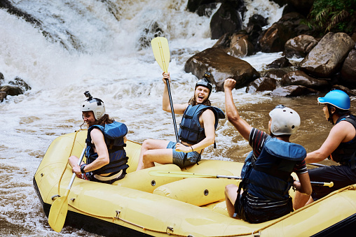 Shot of a group of cheerful young men in a rubber boat celebrating on making through a challenge outside during the day