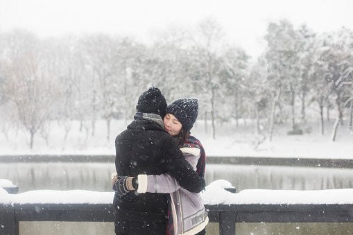 young couple standing on a snow-covered wooden bridge,China.