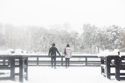 young couple standing on a snow-covered wooden bridge,China.