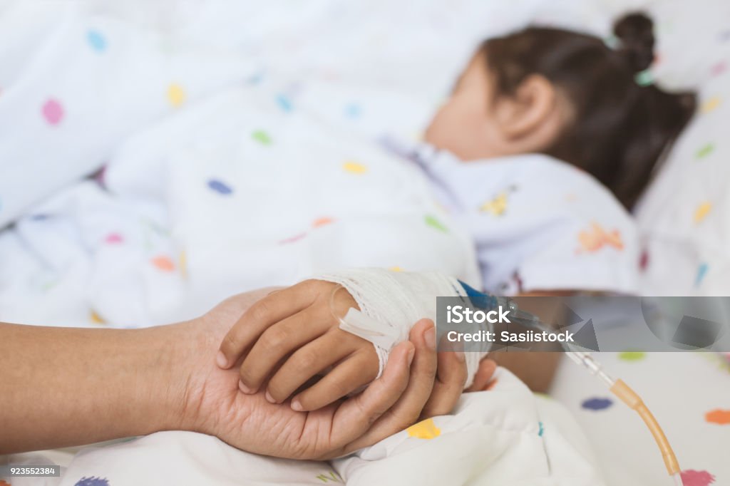 Mother hand holding sick daughter hand who have IV solution bandaged with love and care Mother hand holding sick daughter hand who have IV solution bandaged with love and care while she is sleeping on bed in the hospital Child Stock Photo