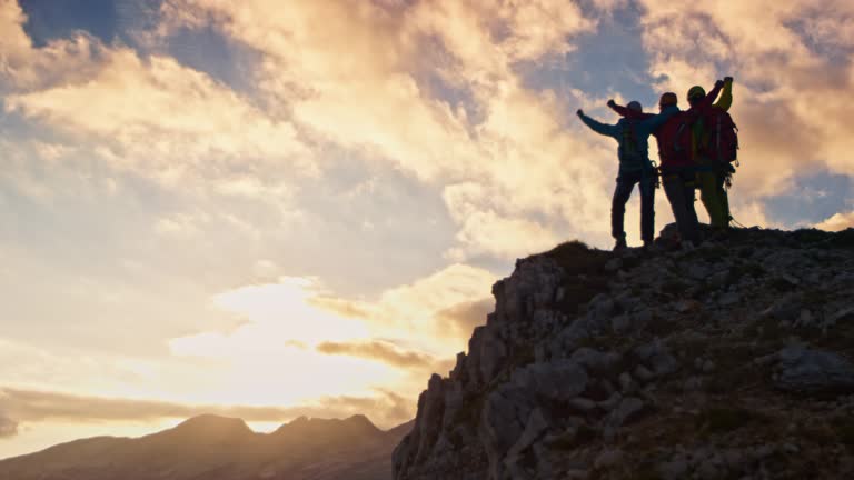 Three mountaineers doing a high five on mountain top at sunset