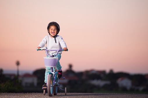 4 years old toddler riding a purple bicycle at sunset time, looking over the camera with a smile.