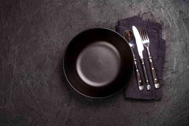 istock Empty black plate and silverware on dark stone backgroun. Top view 923565592