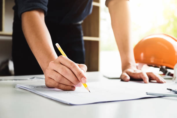 istock Young engineers using yellow pencil of drawing house building structure  before presenting it at the conference with house model, helmet and 923568818