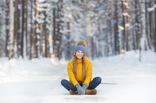 Young smiling woman in a bright clothes sits on a road in a winter forest