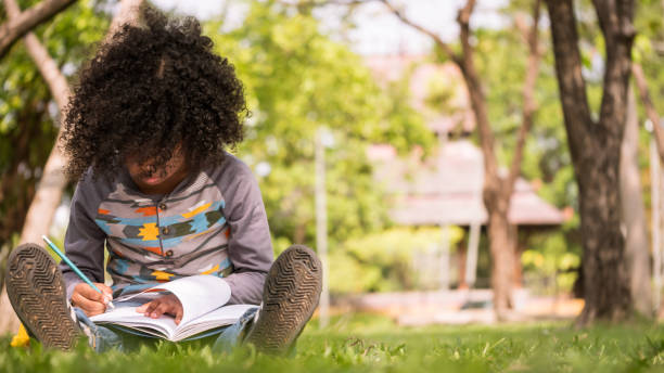 istock A little boy writing on notebook while sitting on green grass in a park 923575214