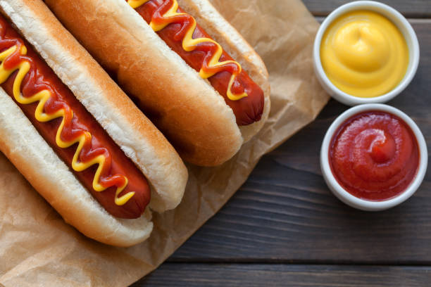 barbecue grilled hot dog with yellow mustard on wooden table - hot dog imagens e fotografias de stock