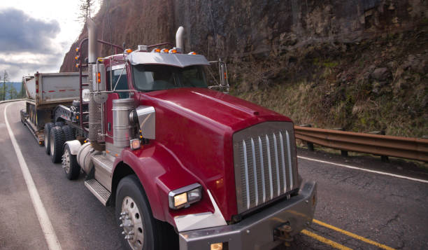 istock Classic red big rig semi truck with step down semi trailer transporting equipment on meandering mountain road 923585702