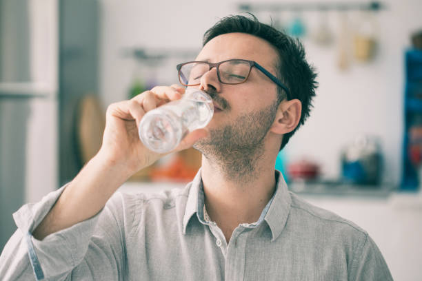 istock Young man drinking water from bottle in kitchen 923597460
