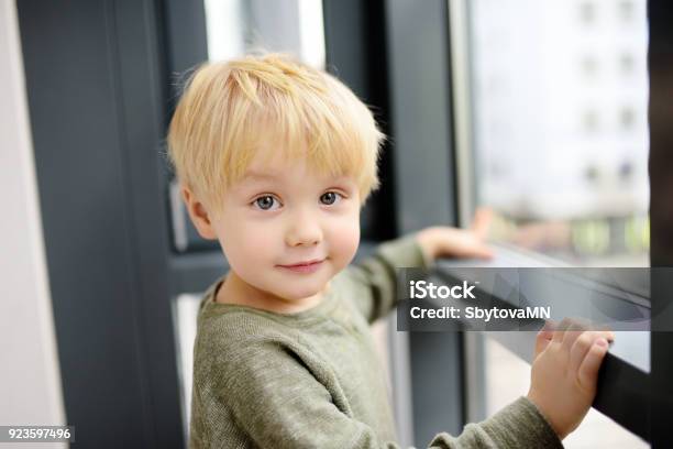 Lovely Little Boy Sitting On The Window Near Panoramic Window And Looking Outside Stock Photo - Download Image Now