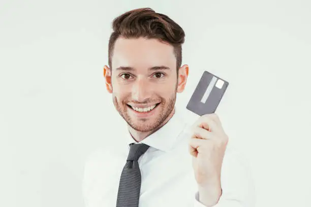 Cheerful successful cardholder using cashless payment. Optimistic handsome young businessman showing black credit card and looking at camera. Cashless environment concept