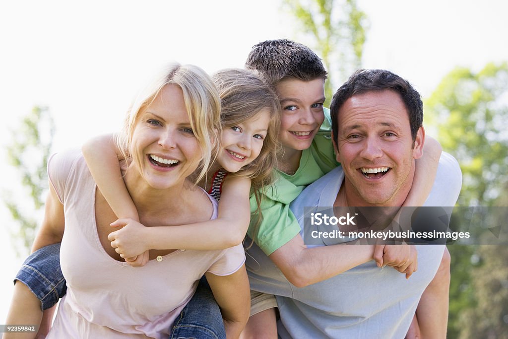 Couple giving two young children piggyback rides Couple giving two young children piggyback rides smiling Family Stock Photo