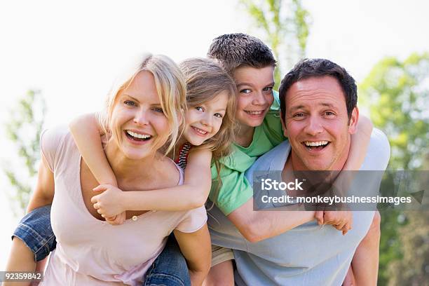 Couple Giving Two Young Children Piggyback Rides Stock Photo - Download Image Now - Family, Mature Couple, Smiling