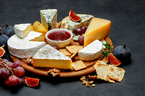 Various types of cheese - parmesan, brie, roquefort, cheddar on wooden cutting board