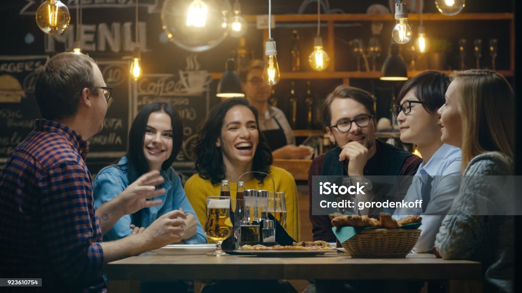 Diverse Group of Young People Have Fun in Bar, Talking, Telling Stories and Jokes. They Drink Various Drinks. They're in the Stylish Hipster Establishment. Discussion Stock Photo