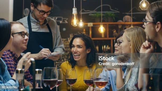 In The Bar Restaurant Waiter Takes Order From A Diverse Group Of Friends Beautiful People Drink Wine And Have Good Time In This Stylish Place Stock Photo - Download Image Now