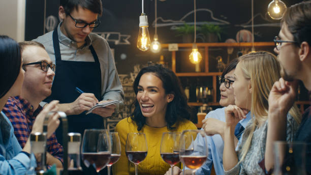 in the bar/ restaurant waiter takes order from a diverse group of friends. beautiful people drink wine and have good time in this stylish place. - job orders imagens e fotografias de stock