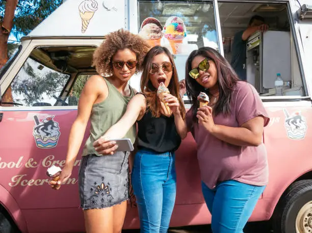 Photo of Three girls eating ice creams near the ice cream truck in Australia