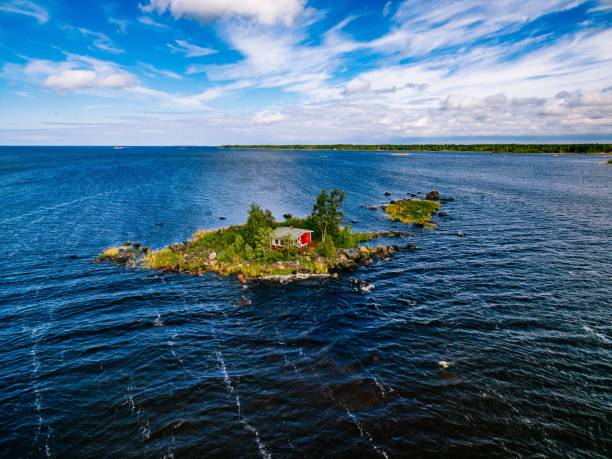 Photo of A small red cottage on an island in the blue sea on a summer day. Finland. View from above.