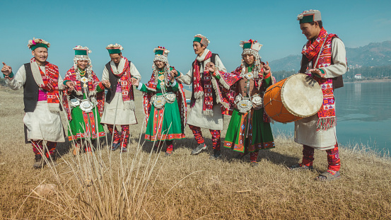 Group of Asian, Indian folk tribal musician and dancers of Kinnaur, Himachal Pradesh. They are singing and dancing together on drum beats of the tribal drummer in group near river. They are in their traditional formal dress and jewelry. Shoot location Bilaspur, India.