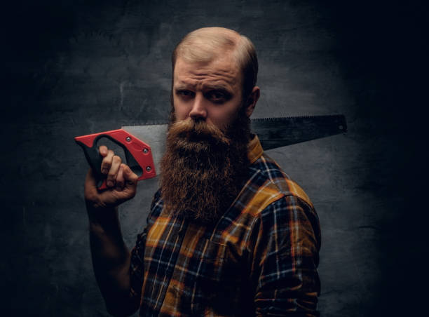 istock A bearded carpenter man dressed in a plaid shirt holds handsaw. 923626926