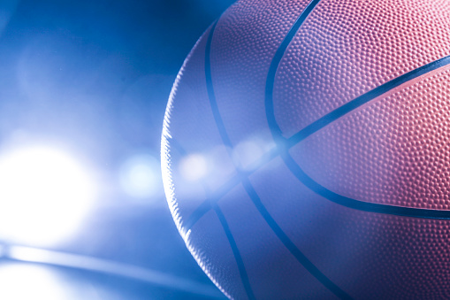 Close-up of orange basketball ball with blue back light.
