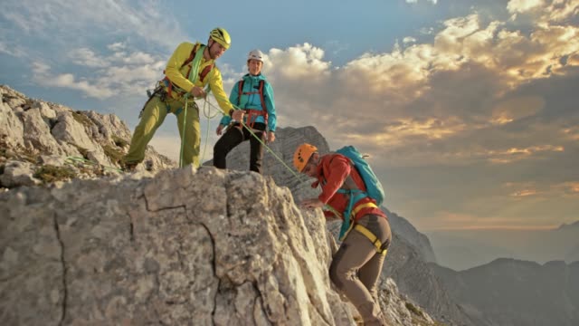 Male mountaineer reaching the top of mountain and celebrating with his two colleagues