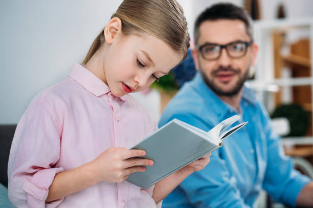 istock selective focus of father looking at daughter reading book 923643296