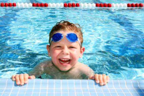 Portrait of smiling little boy enjoying underwater swim in the pool. The boy is gliding by the camera during swimming lesson. Sunny summer day.