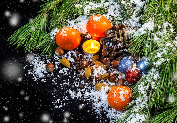 gałęzie sosny, świeca, ozdoby choinkowe, mandarynki, orzechy, stożek sosny w śniegu na czarnym tle - pine nut tree pine tree pine cone zdjęcia i obrazy z banku zdjęć