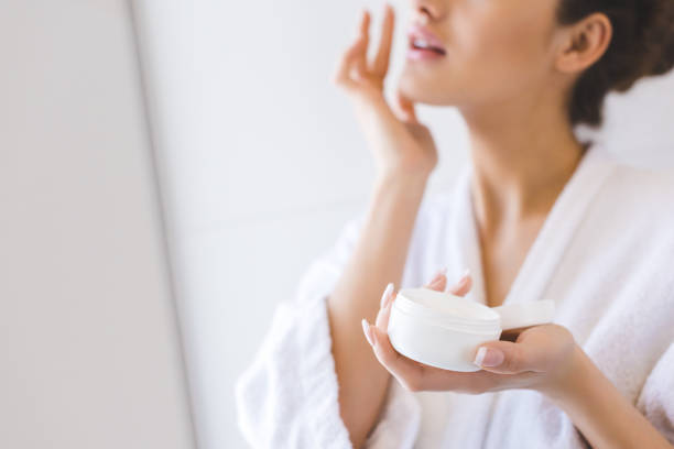 cropped shot of beautiful woman in bathrobe applying face cream - applying imagens e fotografias de stock