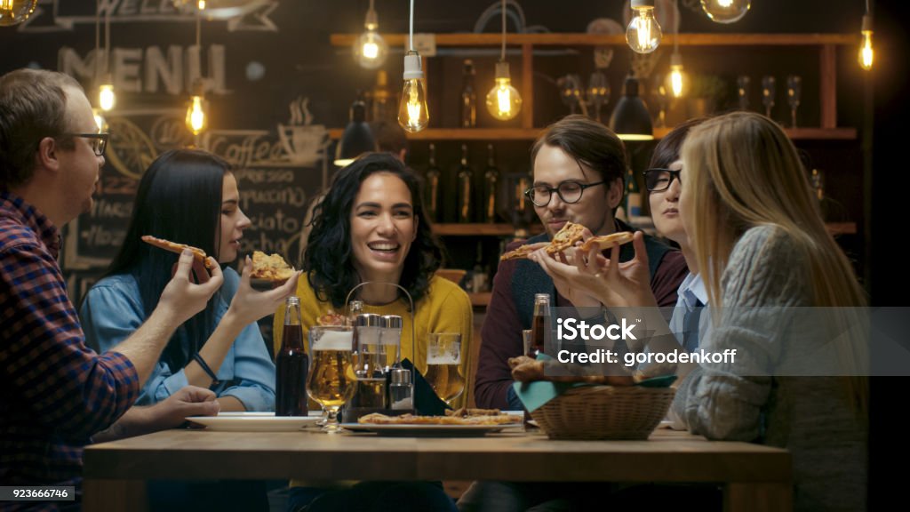 En el Bar / restaurante grupo de diversos jóvenes comer rebanadas de Pizza pastel. Hablar, contar chistes y divertirse en este elegante establecimiento. - Foto de stock de Restaurante libre de derechos