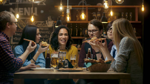 바에서 / 레스토랑 그룹의 다양 한 젊은 이들이 먹는 피자 파이의 조각. 그들은 이야기, 농담 하 고이 세련 된 설립에서. - pub friendship adult party 뉴스 사진 이미지