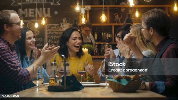 In The Bar Restaurant Beautiful Hispanic Woman Shares Good News With Her Dear Friends They Congratulate Her Heartily And Applaud They Sit In The Stylish Hipster Establishment Stock Photo - Download Image Now