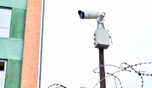 istock Camera video surveillance on the building background mounted on a brick wall, fenced with barbed wire 923667254
