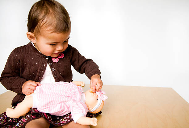 Cute smiling little girl playing with her toy carriage and doll at home