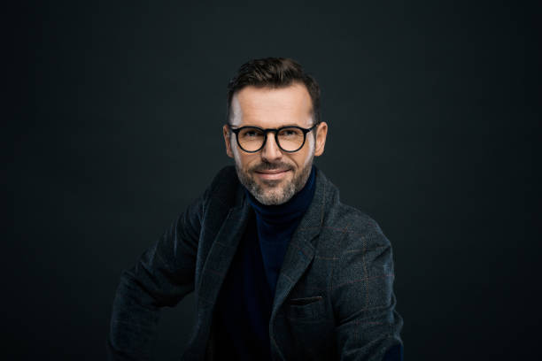 Studio portrait of elegant man, dark background Portrait of handsome businessman in tweed jacket and glasses against black background, smiling at camera. charming photos stock pictures, royalty-free photos & images