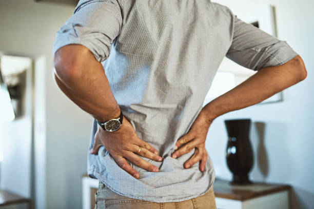 There's a bit of pain at my lower back Rearview shot of an unrecognizable man holding his back in discomfort due to pain inside at home bad posture stock pictures, royalty-free photos & images