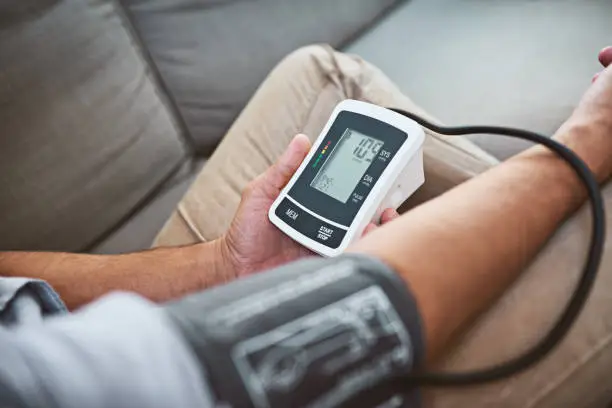 Closeup of an unrecognizable man doing a reading of his blood pressure with a blood pressure monitor while being seated on a couch at home