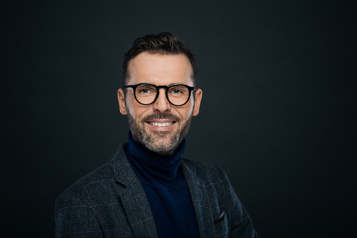 Portrait of handsome businessman in tweed jacket and glasses against black background, smiling at camera.