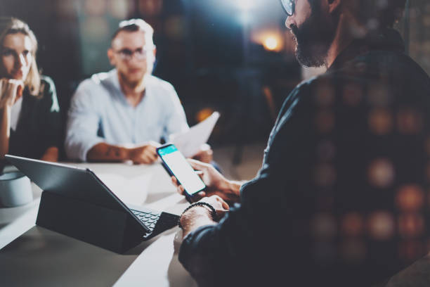 istock Coworkers working together in modern office.Bearded man talking with colleague and using mobile laptop while sitting at the wooden table.Horizontal.Blurred background.Flares. 923684804