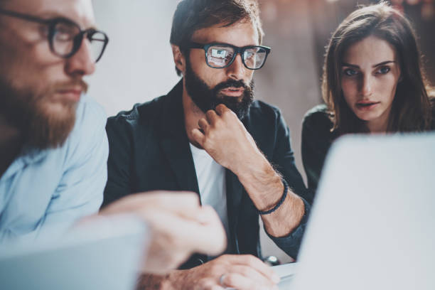 istock Three young coworkers working together on laptops at modern coworking studio at night.Man wearing glasses using laptop.Horizontal.Blurred background. 923684940