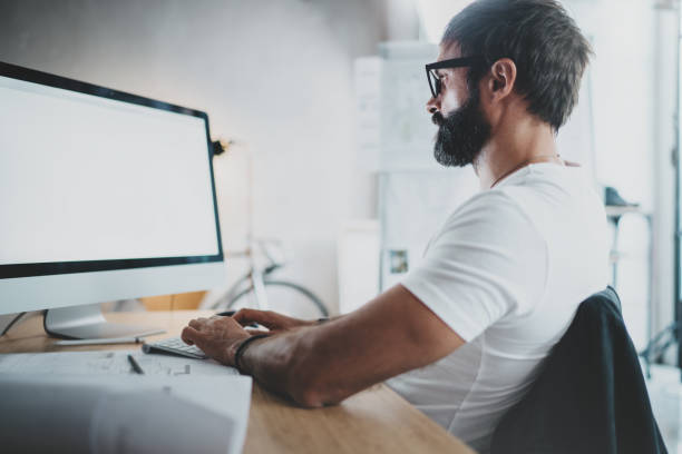 istock Handsome bearded professional architect wearing eye glasses working at modern loft studio-office with desktop computer.White blank display screen.Blurred background. Horizontal. 923691400