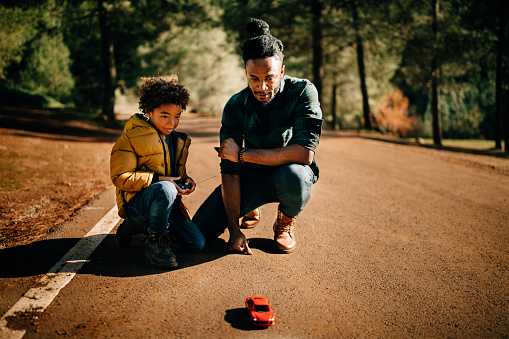 Young father and son using remote control and playing with toy car in the countryside