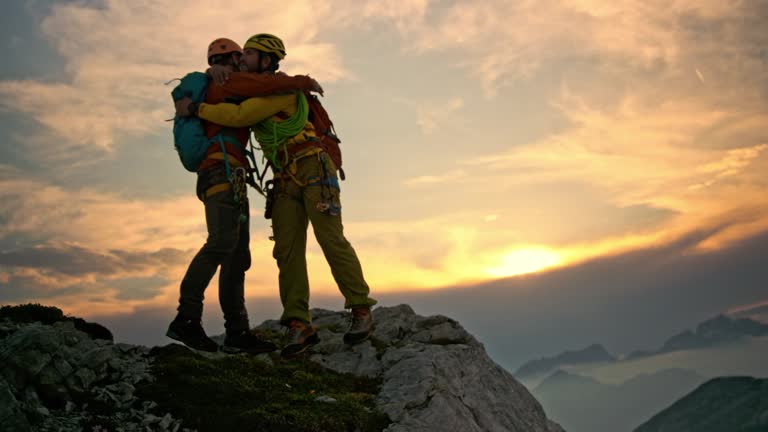 Male mountaineer extending his hand and helping friend get to the mountain top at sunset