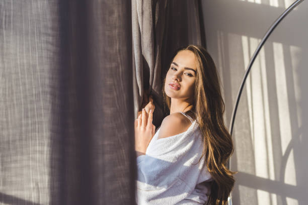 istock pretty pensive woman in bathrobe standing at window at home 923710366