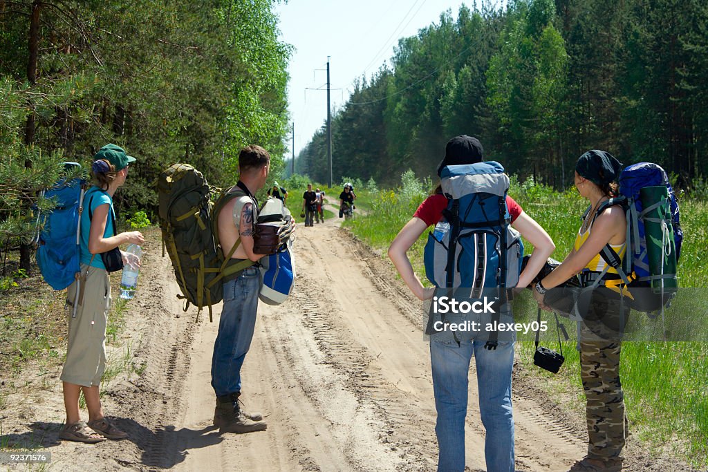 Tourists at wood Four tourists waiting another four at road. Backpack Stock Photo