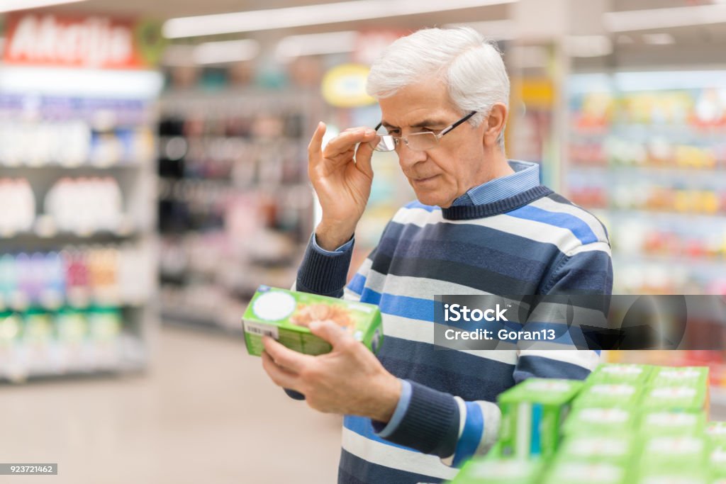 Senior man reading food label at a grocery store Elderly man shopping in local supermarket. He is holding box and reading nutrition label. Nutrition Label Stock Photo